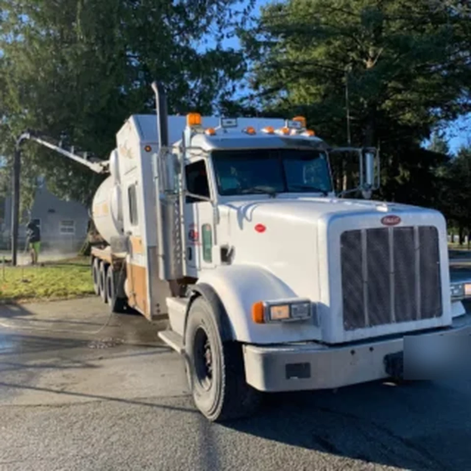 Vacuum service truck arriving along a tree-lined rural property access road.