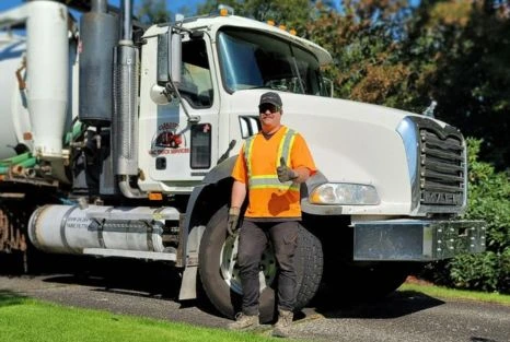 Service technician standing beside branded vacuum truck equipment.